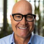 Bald, smiling man with glasses and blue shirt